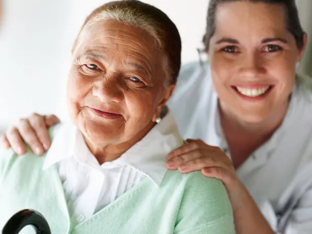 Smiling caregiver with her hands on an elderly woman's shoulders