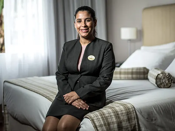House manager in a dark suit sitting in a tidy bedroom, smiling